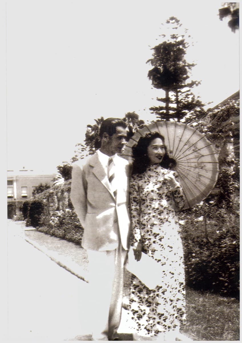 A couple walking a garden path, she carrying a parasol