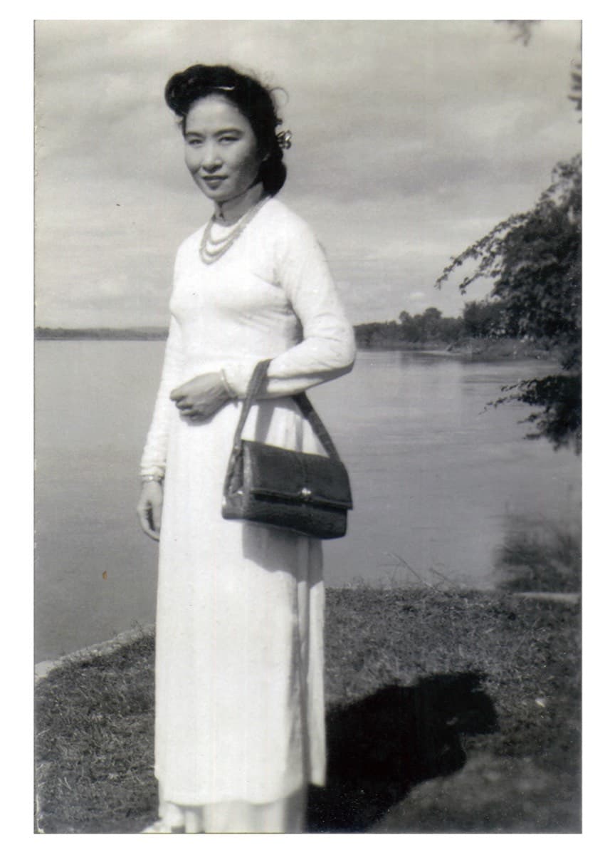 Madame Hoa Ly in a white ao dai on a riverbank, the Mekong behind her
