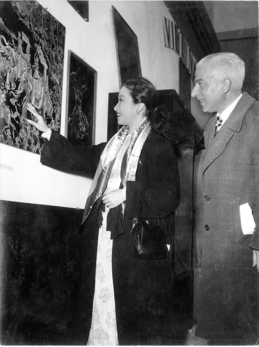 Madame Hoa Ly gesturing towards a lacquer panel on an exhibition wall