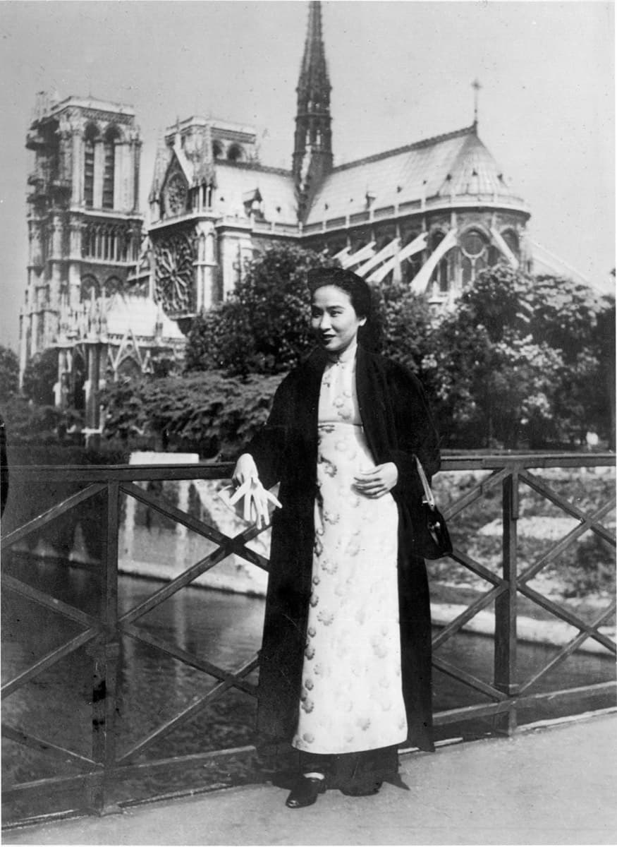 Madame Hoa Ly on a bridge rail, Notre-Dame de Paris behind her