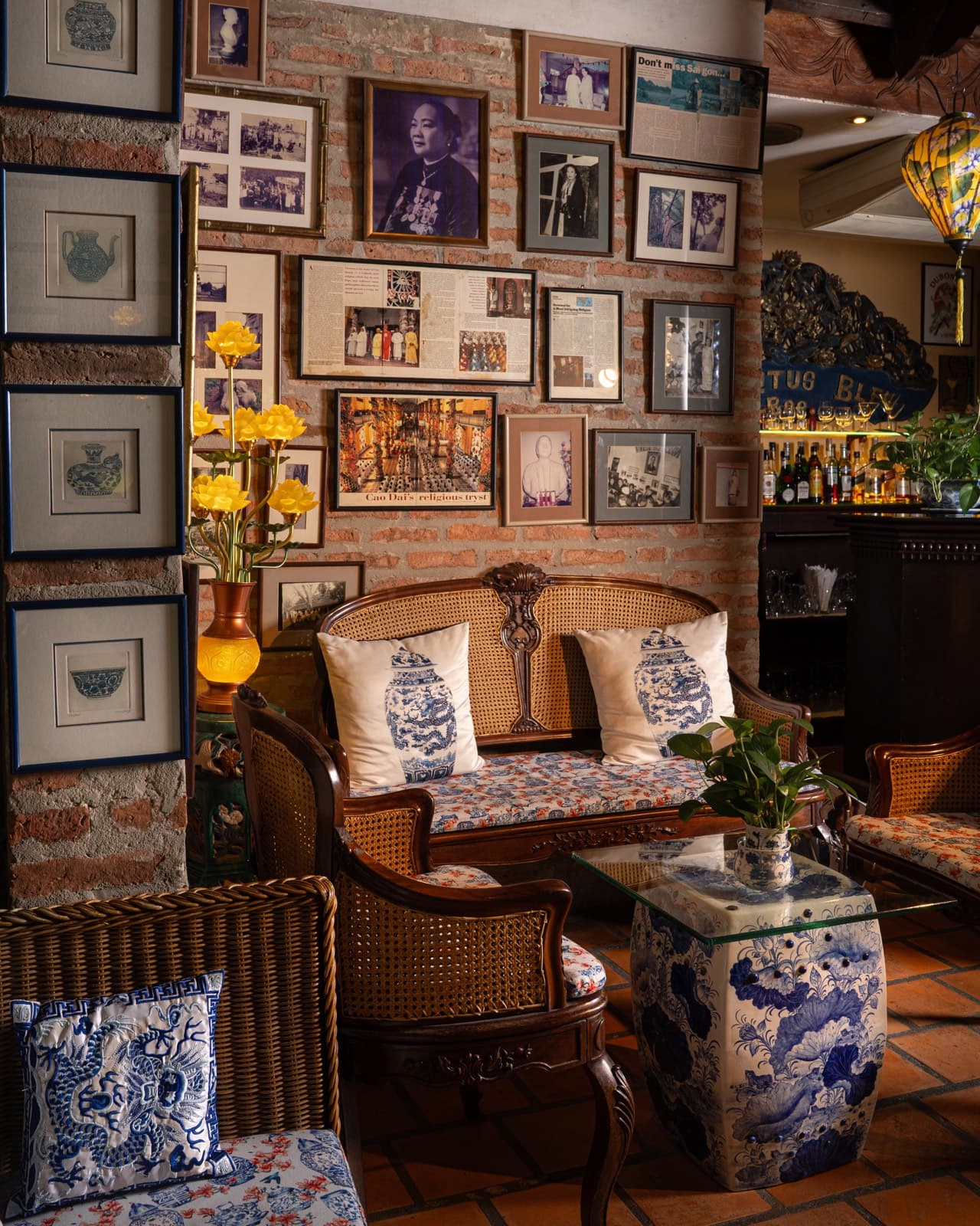 A brick wall inside the villa hung densely with framed family photographs, above a carved settee and blue-and-white porcelain